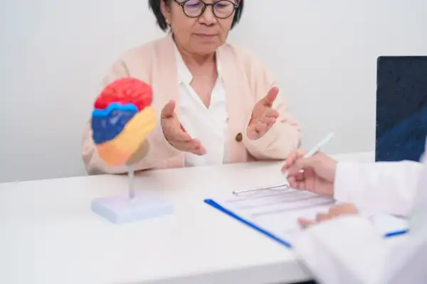Une femme âgée discute avec un médecin, un modèle de cerveau coloré sur la table, suggérant un test de mémoire et concentration.