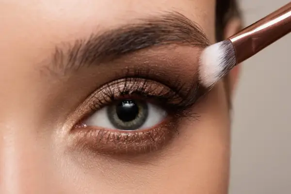 Occhio con trucco elegante, sfumature bronze e un pennello che applica l'ombretto.