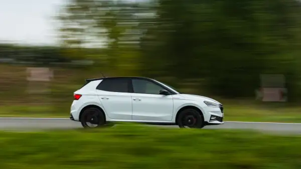 Un Skoda Fabia 130 blanco con techo negro se mueve rápido por una carretera rural, con el paisaje difuminado por la velocidad.