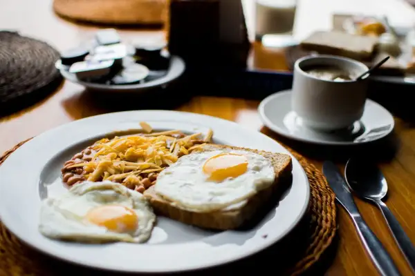 Un petit déjeuner sportif : œufs au plat, haricots et fromage râpé sur une assiette, avec une tasse de café à côté.