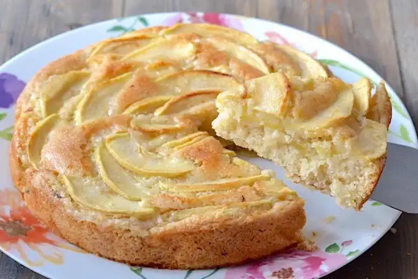 Una fetta di torta di mele senza uova, con mele a fette disposte a spirale sulla superficie dorata.