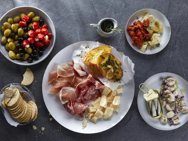 Plateau de charcuterie, fromages, olives, tomates séchées, artichauts, toasts à l'ail et sardines. Une recette antipasti italien facile pour un apéritif gourmand.