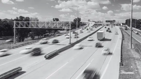 Rozmyte samochody pędzą po wielopasmowej autostradzie. Widoczny znak drogowy i wiadukt. Specustawa drogowa w akcji.