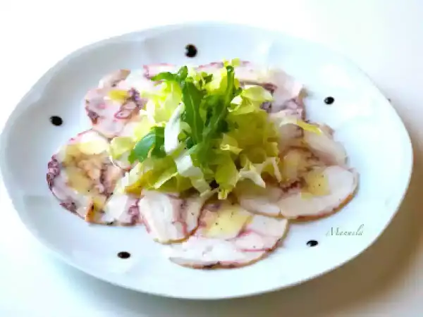 Delicato carpaccio di polpo, affettato sottile e condito con olio e limone, guarnito con insalata fresca e gocce di aceto balsamico.