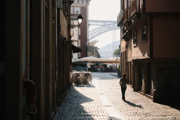 A lone figure walks down a sun-drenched cobblestone street in a European city, a perfect scene for street photography.
