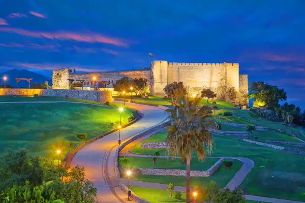 Castillo Sohail iluminado al atardecer, un lugar imprescindible que ver en Fuengirola. Caminos serpenteantes y palmeras bajo un cielo azul intenso.
