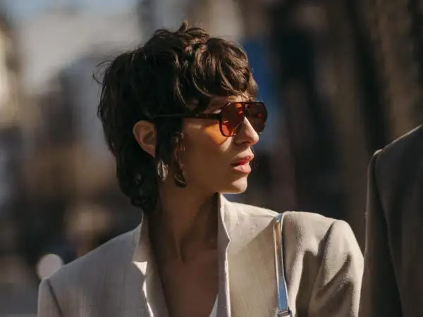 Frau mit einem frechen Pixie Cut, Sonnenbrille und Blazer.