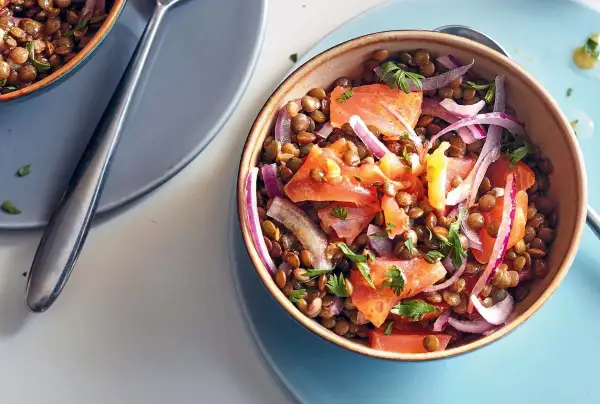 Salade de lentilles aux tomates, oignons rouges et saumon fumé, garnie de persil frais. Un plat coloré et savoureux.