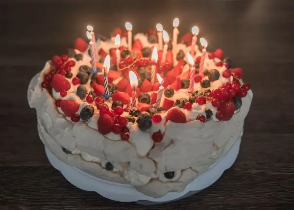 Pyszne ciasto urodzinowe Pavlova ozdobione bitą śmietaną i świeżymi owocami, z płonącymi świeczkami.
