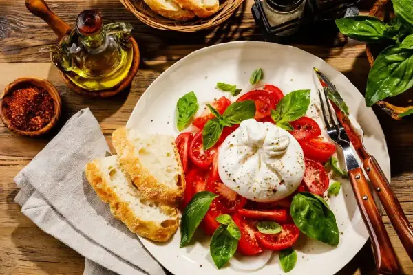 Ser burrata z pomidorami i bazylią, podany z chrupiącym pieczywem. Idealny pomysł na to, ser burrata z czym jeść.