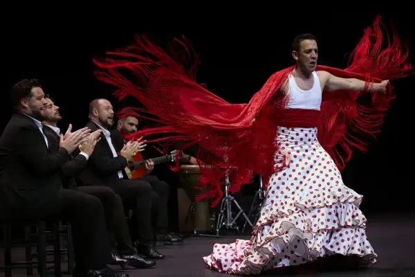 Antonio, cantante flamenco, baila con pasión, su mantón rojo ondea mientras los músicos le acompañan.