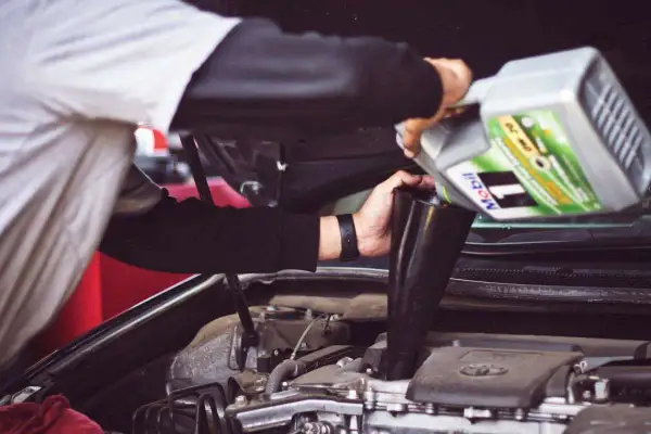 Un meccanico versa olio motore Mobil 1, con specifica API SN, nel vano motore di un'auto.