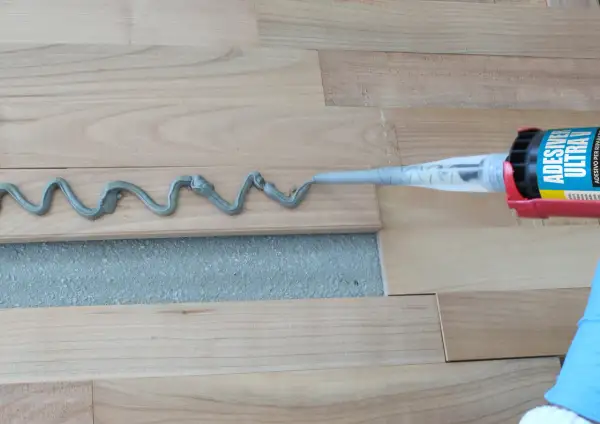 Aplicando adhesivo para parquet con pistola. Preparando para barnizar parquet.