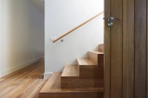 Escalier en bois clair, parfait pour un entretien facile. Une porte en bois sombre s'ouvre sur la cage d'escalier.