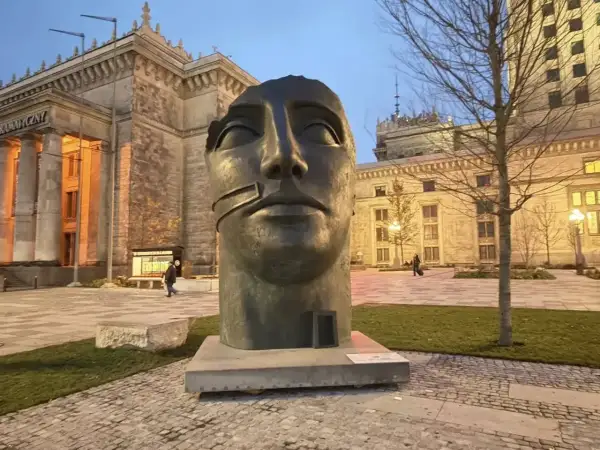 Głowa rzeźby Igora Mitoraja "Luci di Nara" na tle Pałacu Kultury i Nauki w Warszawie.