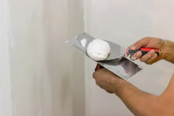 Mani che usano una spatola per applicare lo stucco bianco su un muro.