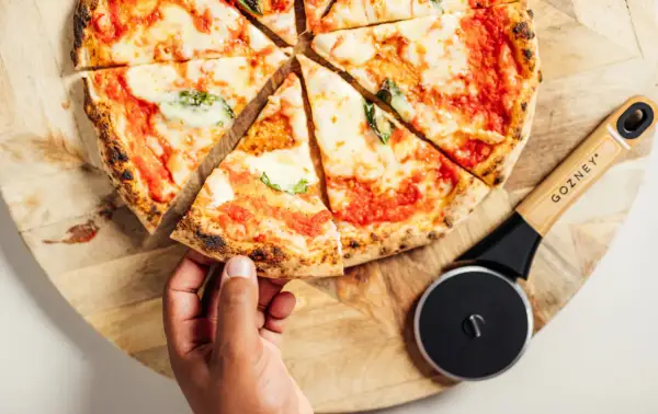 Une main prend une part de pizza maison, fraîchement coupée, prête à être dégustée. Idéal pour congeler pizza maison et en profiter plus tard.