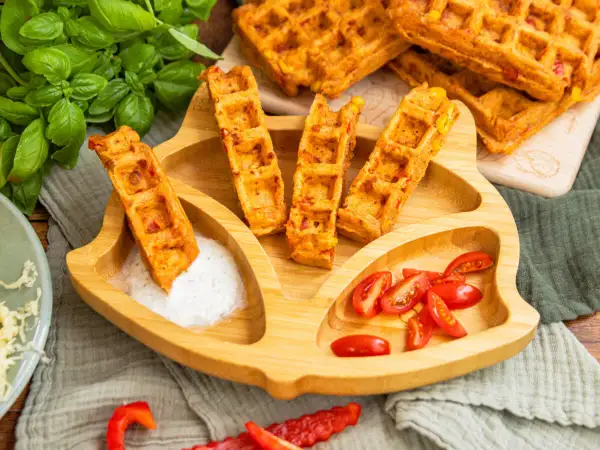 Leckere Pizza-Waffeln mit Mais und Paprika, serviert auf einem Kinder-Teller mit Tomaten und Dip. Ein Hit für kleine Feinschmecker!