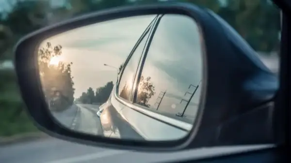 Widok z lusterka bocznego Toyoty. Słońce odbija się w szybie, a droga wije się w oddali.