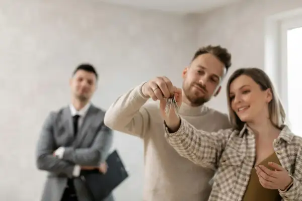 Coppia felice riceve le chiavi di casa, con un agente immobiliare sullo sfondo. Ottima opportunità per la surroga mutuo INPS dipendenti pubblici.