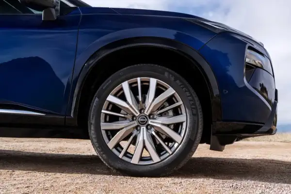 Błękitny Nissan X-Trail na drodze gruntowej, z widocznym kołem i fragmentem nadwozia.