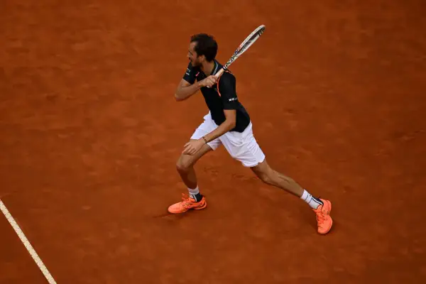 Tenisista wykonuje potężny **backhand** na ceglanej nawierzchni.