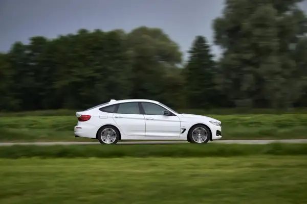 Białe BMW 330d mija zielone pola i drzewa, poruszając się z dużą prędkością.