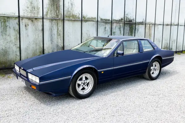 Granatowy Aston Martin Lagonda z lat 80. na tle industrialnej ściany.