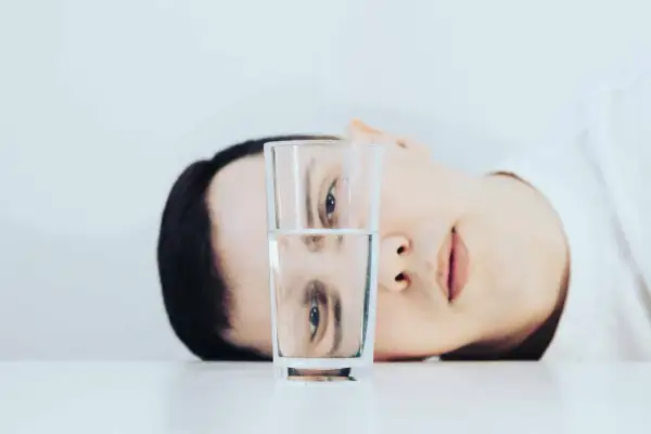 Un rostro se refleja en un vaso de agua, mostrando una dualidad entre el pesimista y el optimista.