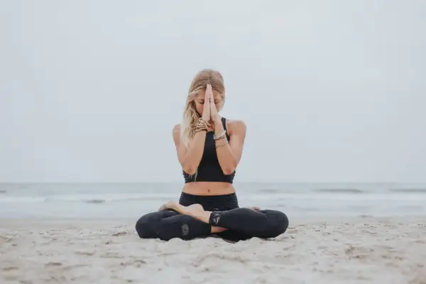 Mujer rubia meditando en la playa, con el gesto namaste. Paz y serenidad en el mar.