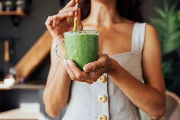 Donna sorseggia un frullato verde, un'ottima opzione su cosa bere per dimagrire.