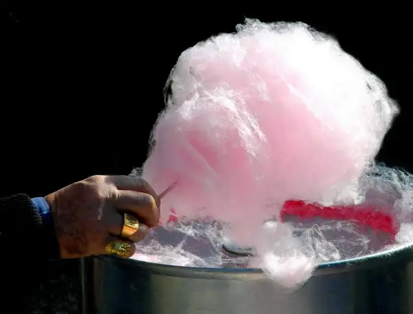 Main d'un homme fabriquant du sucre à barbe à papa rose et blanc.