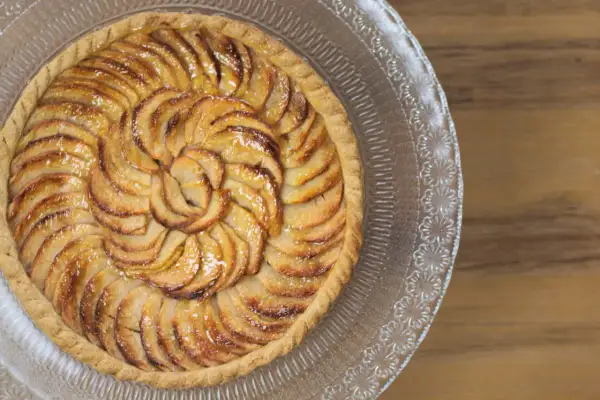 Tarte aux pommes recette : une tarte aux pommes dorée, disposée en spirale sur un plat en verre, prête à être dégustée.