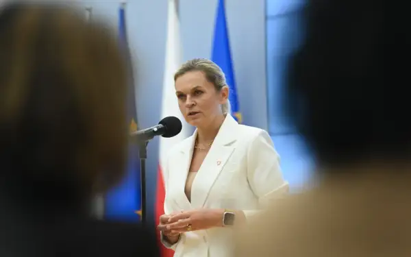 Minister edukacji przemawia przy mikrofonie, w tle flagi Polski i UE.