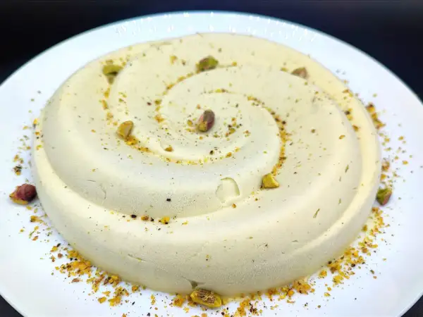 Delizioso semifreddo al pistacchio, decorato con granella e pistacchi interi, servito su un piatto bianco.