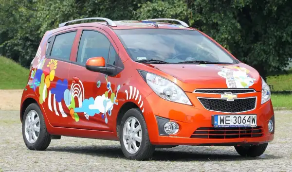 Pomarańczowy Chevrolet Spark 2010 z kolorowymi, abstrakcyjnymi wzorami na karoserii.