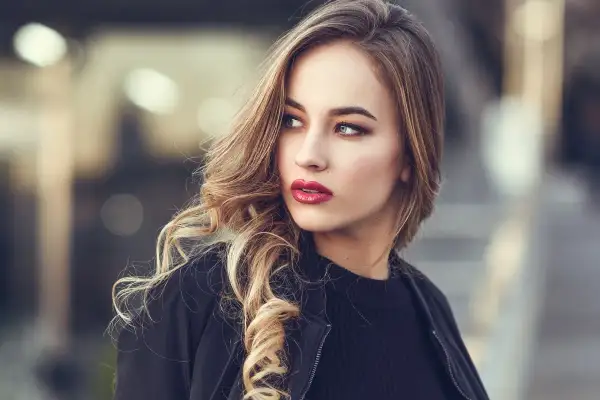 Blondynka z burzą falowanych włosów i wyrazistymi, czerwonymi ustami. Idealny kolor pomadki dla blondynek, który podkreśla urodę.