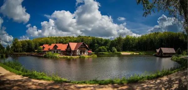 Idealne miejsce na długi weekend w sierpniu: urokliwe domki nad jeziorem, otoczone lasem, z pięknym niebem i chmurami.
