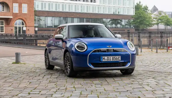 Mini Cooper SE azul aparcado en calle adoquinada, con edificios modernos de fondo. Su autonomía eléctrica inspira libertad.
