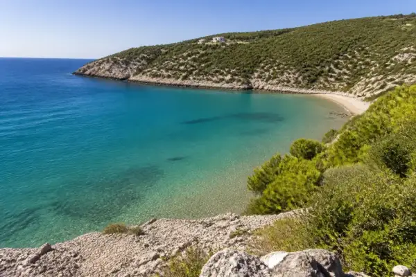 Vista dall'alto della spiaggia di Procinisco, con acque cristalline turchesi che lambiscono una sabbia dorata, incorniciata da colline verdi e rocciose.