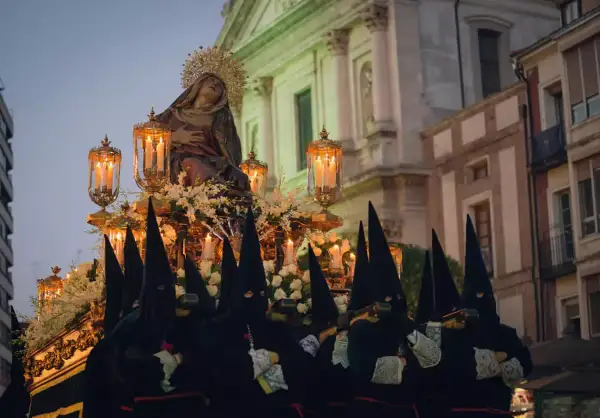 Figuras encapuchadas portan un paso con la Virgen, iluminado por velas, durante las procesiones de Sábado Santo.