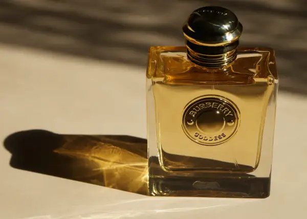 Złota butelka perfum Burberry Goddess, lśniąca w świetle, z wytłoczonym logo.