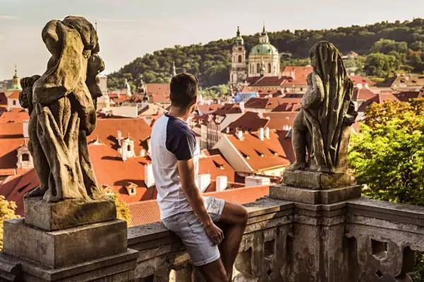 Un homme contemple les toits de Prague, une ville d'Europe aux charmes intemporels, depuis un balcon orné de statues.