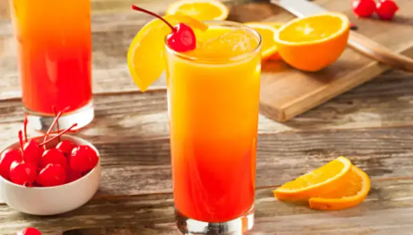 Cóctel refrescante con capas de granadina y naranja, adornado con una cereza y rodajas de naranja.