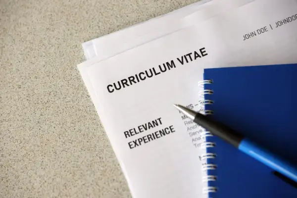 Długopis leży na dokumentach z nagłówkiem "CURRICULUM VITAE". Widoczna jest sekcja "RELEVANT EXPERIENCE" oraz klauzula CV po angielsku.
