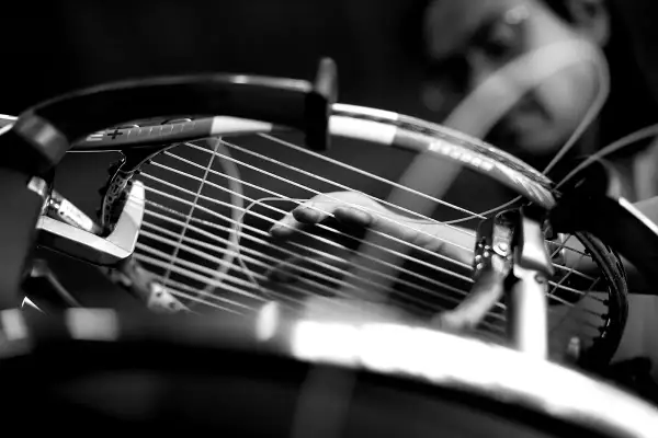 Mano che regola la tensione delle corde di una racchetta da tennis, un dettaglio cruciale per la performance.