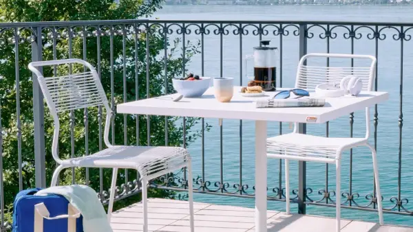 Idee per arredare balcone piccolo: tavolino bianco con caffè, frutta e sedie moderne, vista lago.