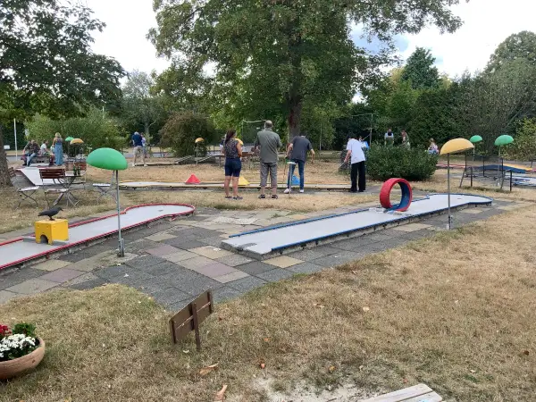 Familien spielen Minigolf Gummersbach. Bunte Bahnen mit Hindernissen wie einem roten Reifen laden zum Spiel ein.