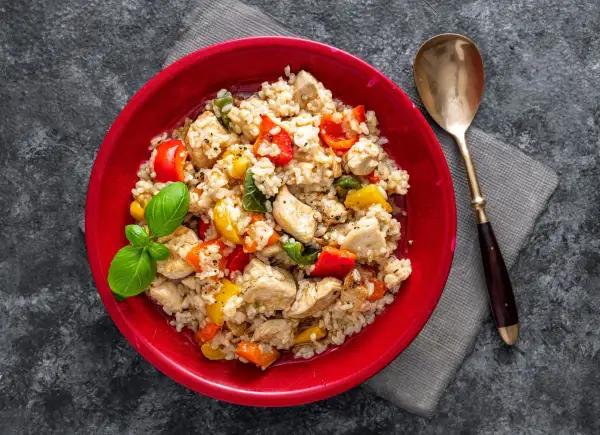 Pyszne risotto z kurczakiem, kolorową papryką i świeżą bazylią, podane w czerwonej misce.