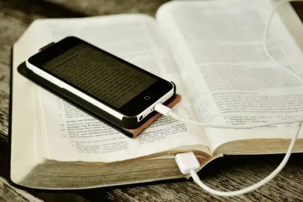 Nowoczesna biblia na co dzień: smartfon z tekstem biblijnym leży na otwartej księdze, podłączony do ładowania.